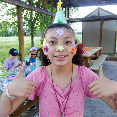 Happy camper girl with a thumbs up for fun. Stickers all over her face.