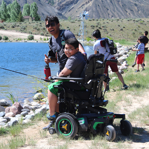 camper in wheelchair with camp counselor fishing at the pond