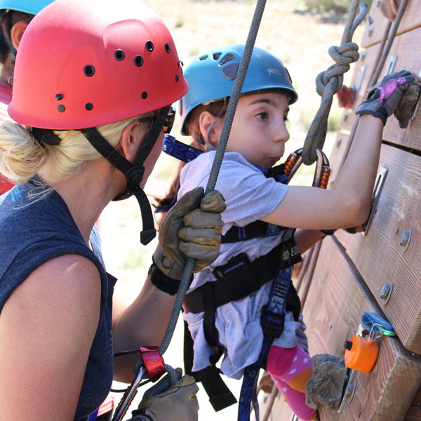 Camper ascending the climbing wall with the help of a camp volunteer.